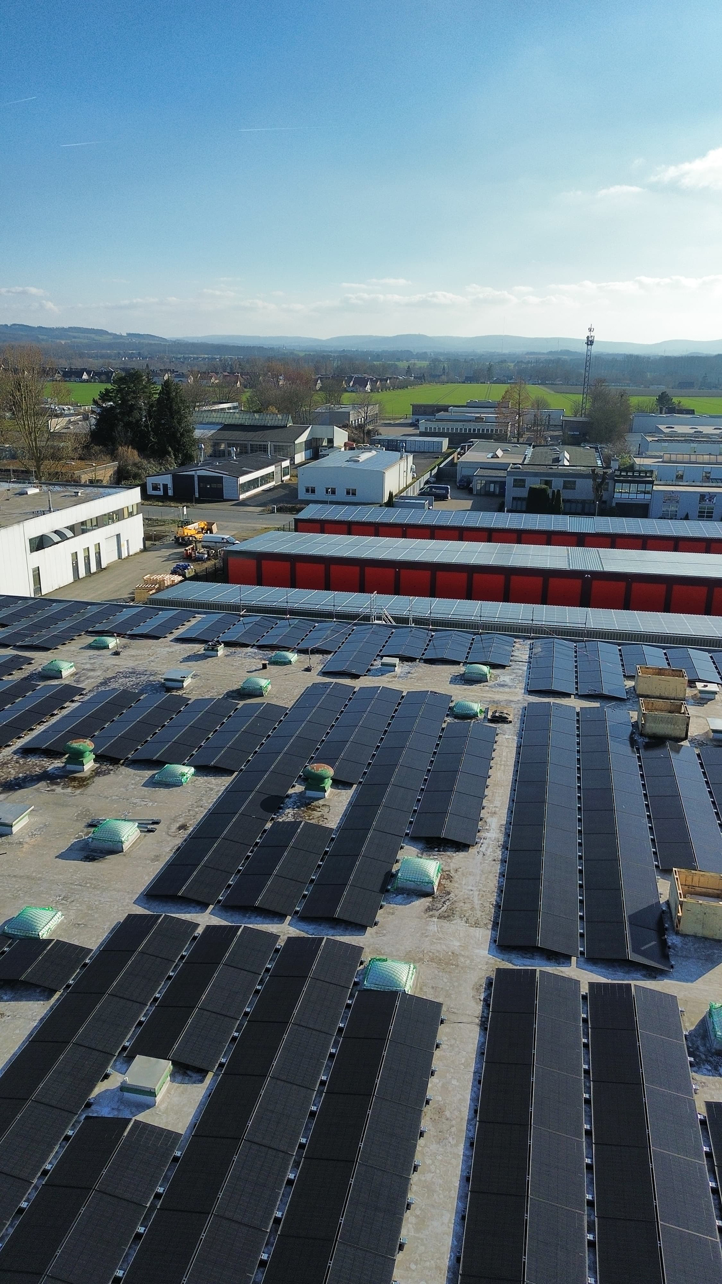 Eine großflächige Solaranlage auf den Dächern eines Gewerbeareals. Die Module sind in langen Reihen montiert und umgeben von Hallen und Betriebsgebäuden.