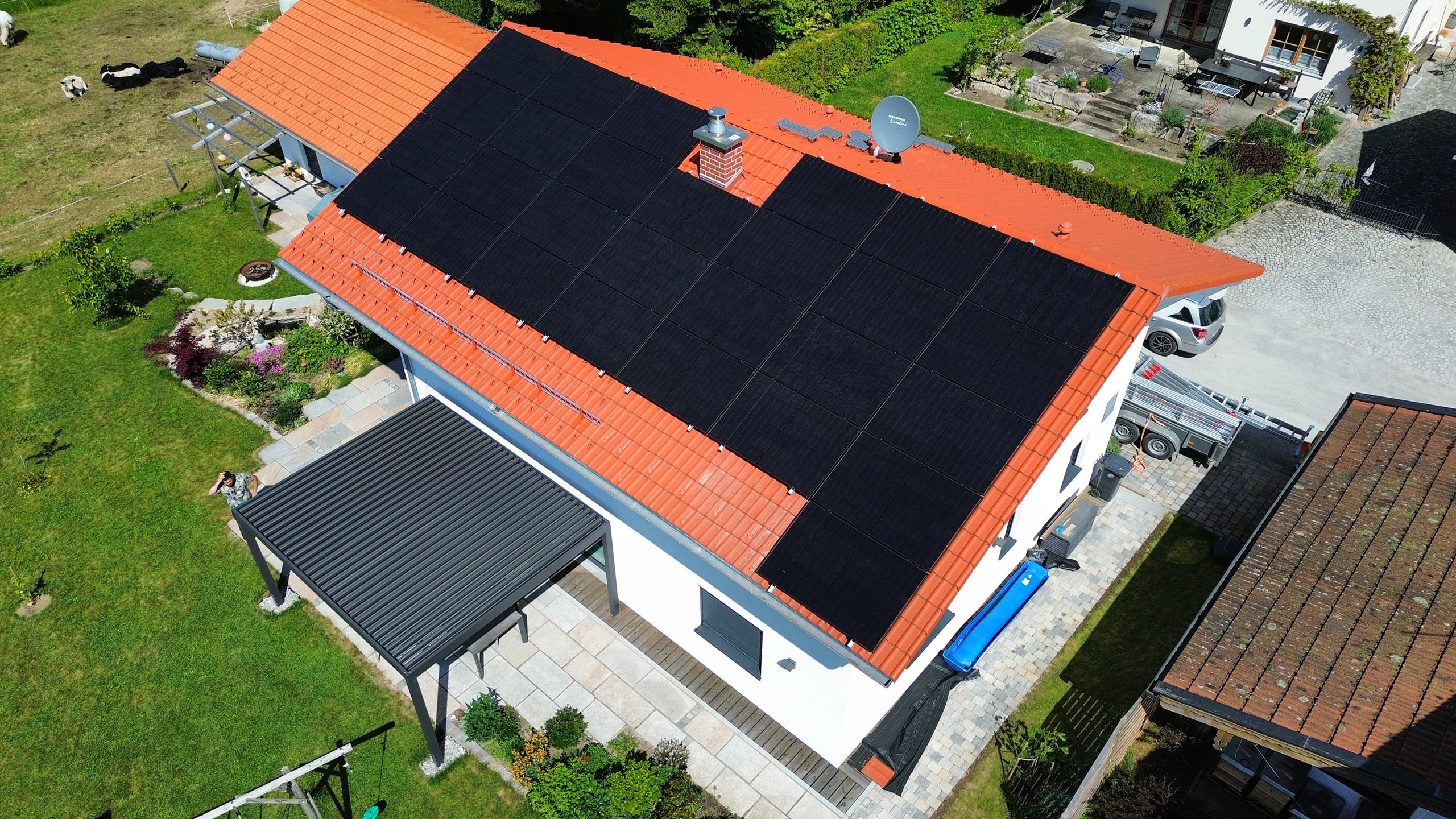 Eine großflächige Photovoltaikanlage auf dem Dach eines Wohnhauses. Der grüne Garten umgibt das Gebäude.